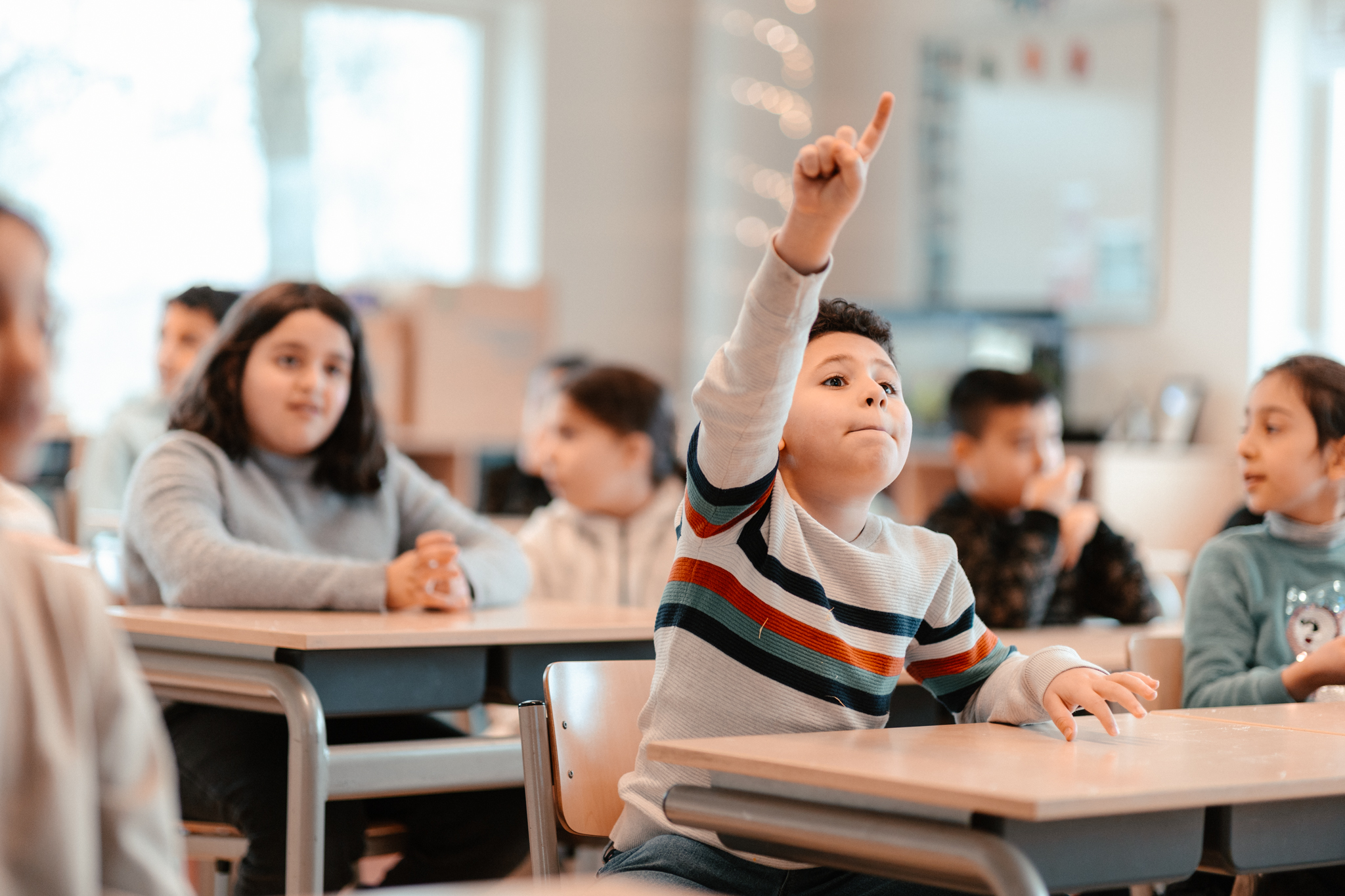 Jongen met hand opgestoken in de klas